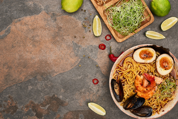 top view of spicy seafood ramen near fresh ingredients on stone surface - Fotó, kép