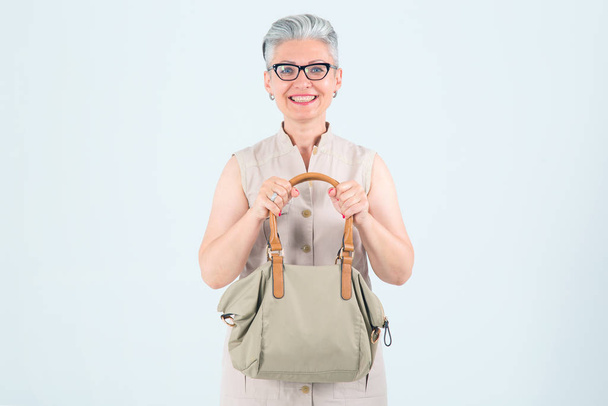 Mulher de meia-idade feliz com um saco de compras, olhando para a frente enquanto está em um fundo leve
. - Foto, Imagem