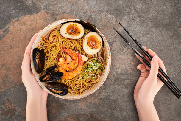 cropped view of woman eating spicy seafood ramen with chopsticks on stone surface - Foto, Imagem
