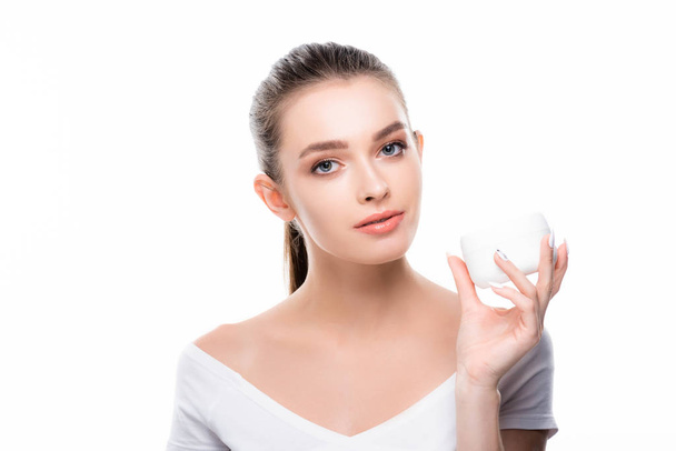 attractive girl looking at camera while holding container with face cream isolated on white - 写真・画像