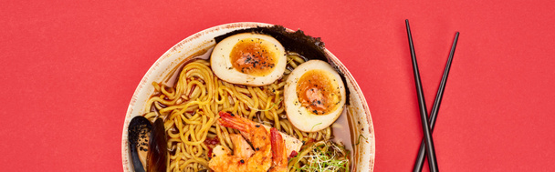top view of spicy seafood ramen near chopsticks isolated on red, panoramic shot - Photo, Image