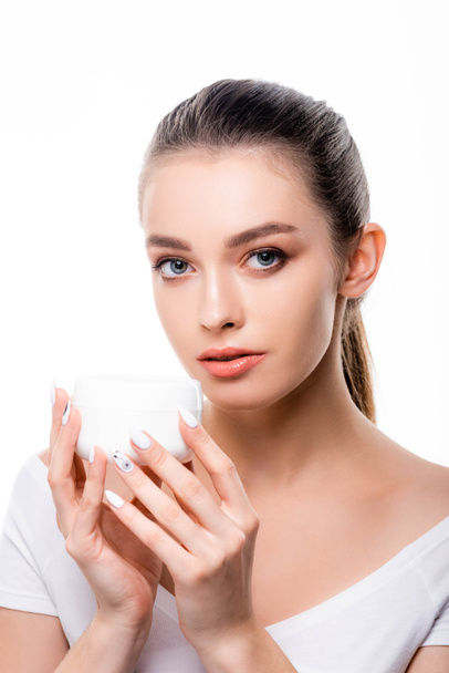 attractive girl looking at camera while holding container with face cream isolated on white - Photo, Image