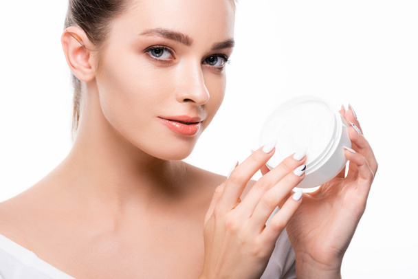 attractive girl looking at camera while touching face cream in container isolated on white - Fotografie, Obrázek