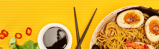 top view of seafood ramen near fresh ingredients, soy sauce and chopsticks on yellow surface, panoramic shot - Photo, Image