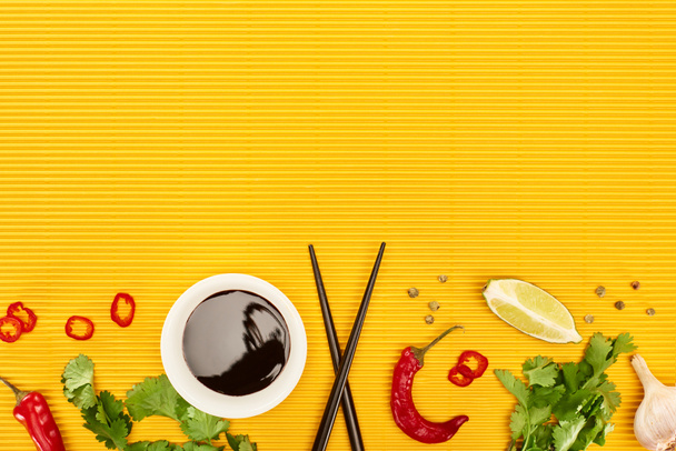 top view of fresh spices, vegetables, soy sauce and chopsticks on yellow surface - Photo, Image