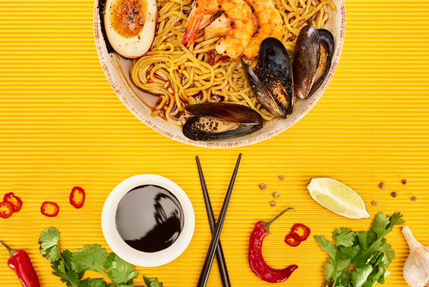 top view of seafood ramen near fresh ingredients and chopsticks on yellow surface - Foto, Bild