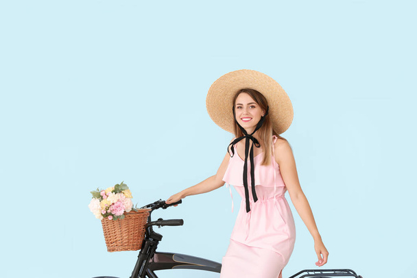 Hermosa mujer joven con bicicleta y ramo de flores de clavel sobre fondo de color
 - Foto, imagen