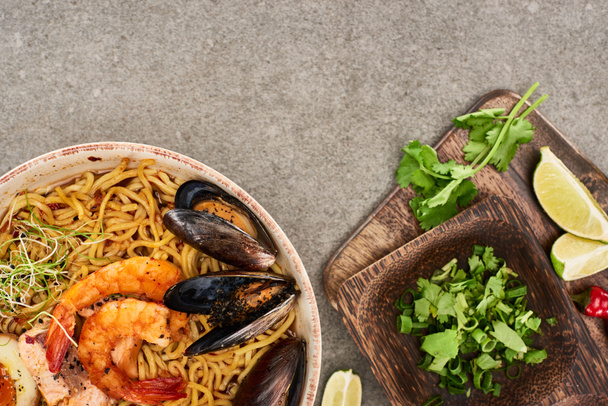 top view of spicy seafood ramen near fresh ingredients on grey surface - Fotó, kép