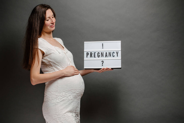 Pregnant woman portrait. She is holding a belly and smiling - Photo, Image