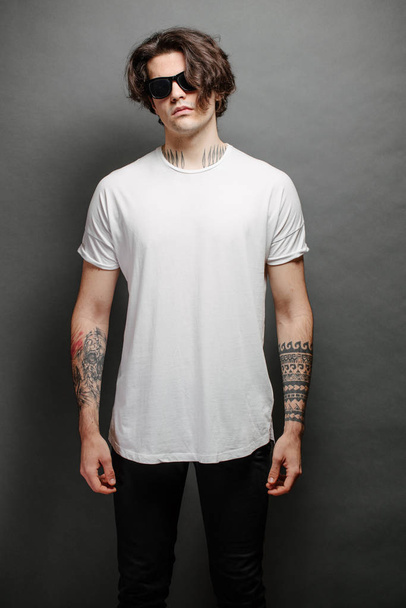 Hipster handsome male model with glasses wearing white blank t-shirt and black jeans with space for your logo or design in casual urban style - Фото, зображення