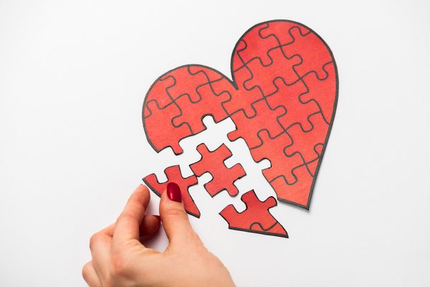 cropped view of woman touching drawn red heart shape jigsaw isolated on white  - Foto, afbeelding