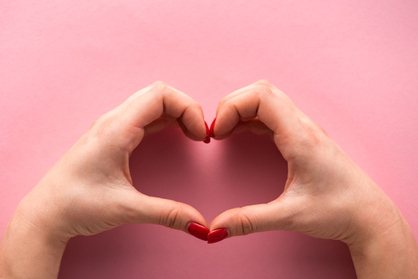 cropped view of woman showing heart-shaped sign with hands on pink  - Foto, imagen