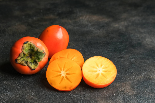 Fresh organic ripe Persimmons fruits  with slice isolated on dark background. Top view. Free copy space. - Zdjęcie, obraz