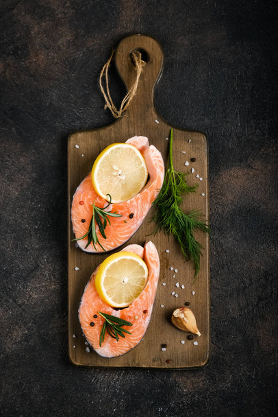 Fresh salmon steaks with herbs, lemon, rosemary and spices on a cutting board on a dark background top view - Fotó, kép