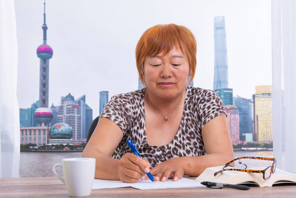 Mujer asiática en la oficina escribiendo en un papel con una pluma
 - Foto, imagen