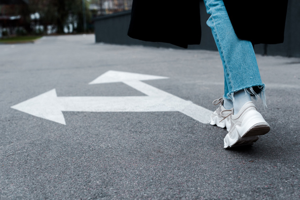 vista recortada de la mujer en jeans caminando cerca de flechas direccionales sobre asfalto
  - Foto, Imagen