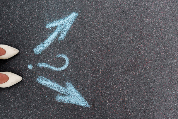 vista superior de la mujer de pie cerca de flechas direccionales y signo de interrogación en asfalto
  - Foto, Imagen