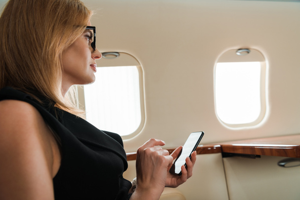 πλαϊνή άποψη της επιχειρηματία που κατέχουν smartphone σε ιδιωτικό αεροπλάνο  - Φωτογραφία, εικόνα
