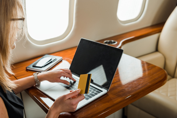 vista recortada de la mujer de negocios con tarjeta de crédito cerca de la computadora portátil en jet privado
  - Foto, Imagen