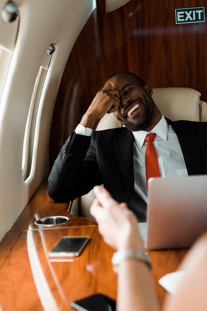 επιλεκτική εστίαση του Αφροαμερικανού επιχειρηματία γελώντας κοντά σε επιχειρηματία σε ιδιωτικό αεροπλάνο  - Φωτογραφία, εικόνα