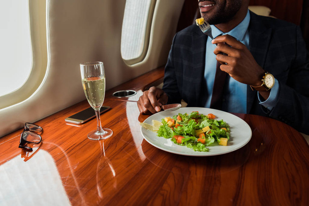 cropped view of african american businessman eating salad in private jet  - Fotografie, Obrázek