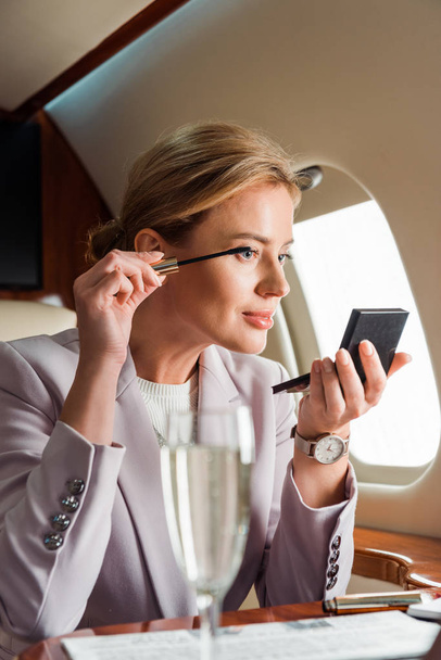 selective focus of businesswoman applying mascara in private plane  - Photo, Image