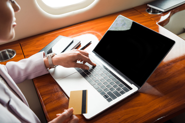 vista recortada de la mujer de negocios utilizando el ordenador portátil con pantalla en blanco y la celebración de la tarjeta de crédito en avión privado
  - Foto, imagen