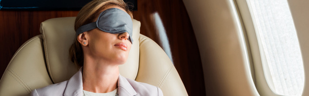 panoramic shot of businesswoman with sleeping mask sitting in private plane  - Photo, Image