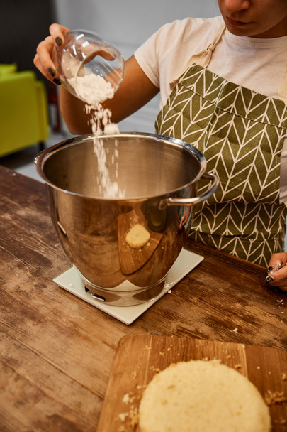 Cropped view of confectioner adding flour in bowl beside biscuit layer on cutting board  - Photo, Image