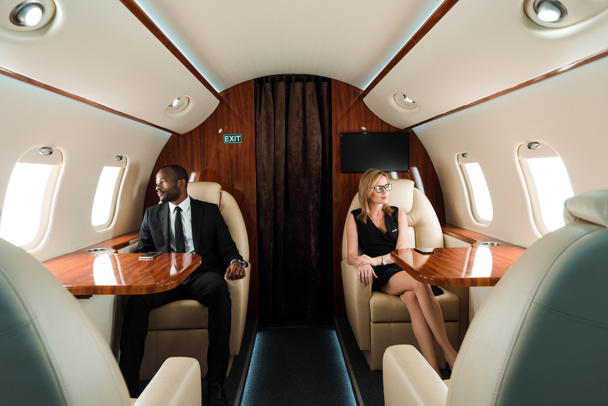 ハンサムなアフリカ系アメリカ人ビジネスマンや民間航空機に座っている魅力的なビジネス女性の選択的な焦点  - 写真・画像