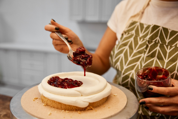 Cropped view of confectioner adding tasty berry jam on cake - Fotó, kép