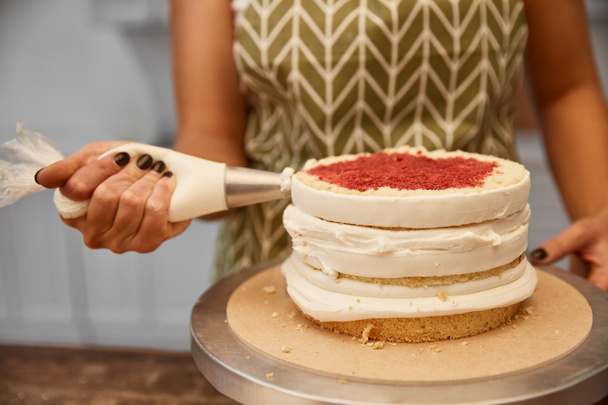 Vista recortada del pastelero usando una bolsa de pastelería con crema mientras hace la torta
  - Foto, Imagen