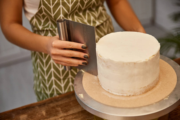 Vista recortada del confitero usando raspador para crema en pastel de esponja
 - Foto, imagen