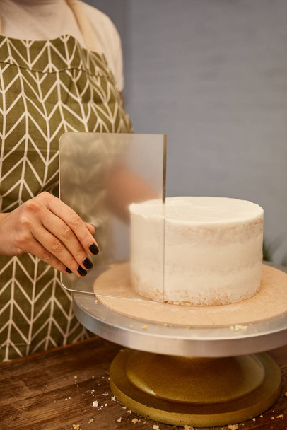 Cropped view of confectioner using transparent scraper on cake cream - Foto, afbeelding