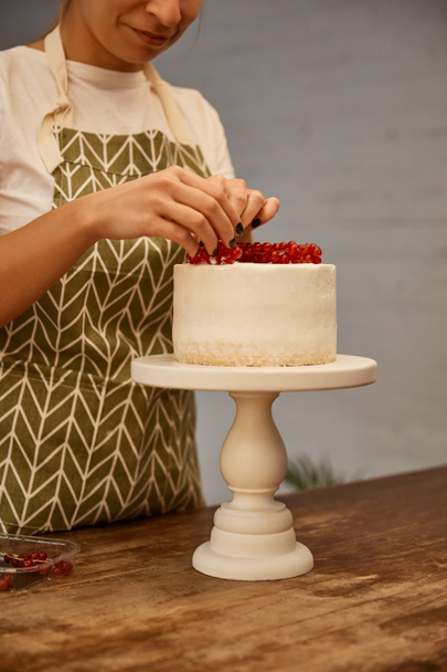 Cropped view of smiling confectioner decorating cake with sweet redcurrant - Fotografie, Obrázek