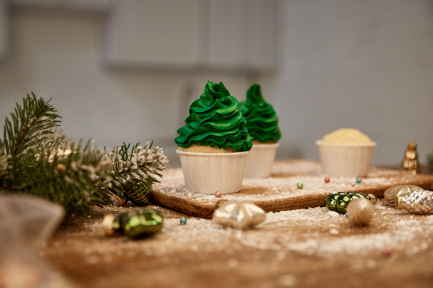 Sabrosos cupcakes con crema verde en la mesa con bolas de Navidad y rama de pino en la mesa
 - Foto, Imagen