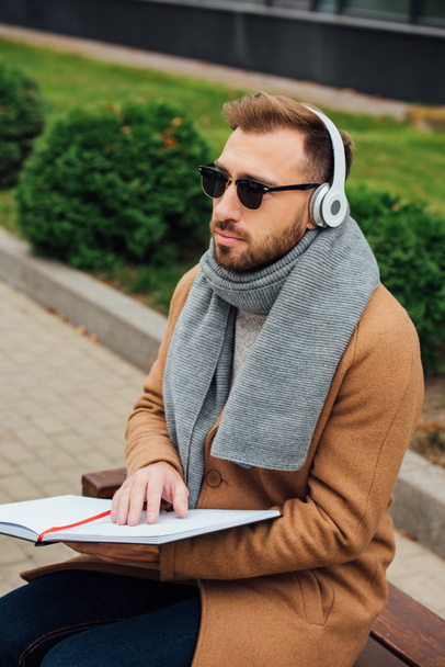 Blind man in headphones reading book with braille font in park - Photo, Image
