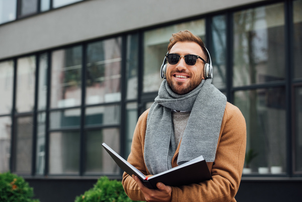 Smiling blind man in headphones holding book on urban street - Foto, imagen