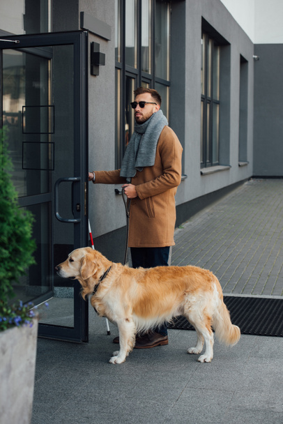 Blind man with guide dog and walking stick opening door of building - Foto, afbeelding