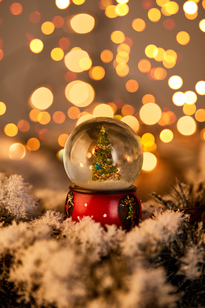 little snowball with christmas tree standing in snow with golden lights bokeh - Photo, Image