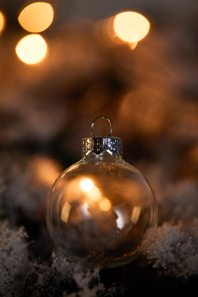 bola de Navidad transparente en ramas de abeto en la nieve con luces amarillas borrosas en la oscuridad
 - Foto, Imagen