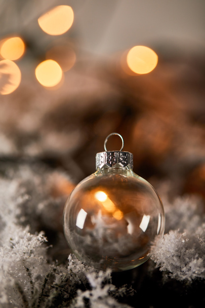 boule de Noël transparente sur les branches d'épinette dans la neige avec des lumières jaunes floues
 - Photo, image