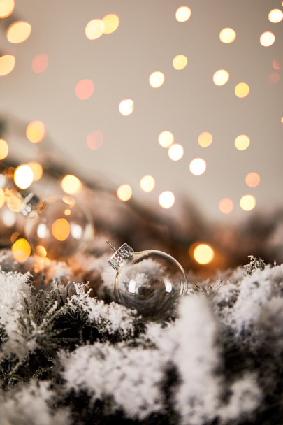transparente Weihnachtskugeln auf Fichtenzweigen im Schnee mit verschwommenem gelben Licht - Foto, Bild