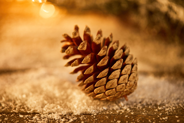 un cono de pino sobre mesa de madera en nieve y luces navideñas bokeh
 - Foto, imagen