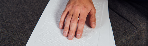 Vista cortada de homem cego lendo braille fonte no sofá, tiro panorâmico
 - Foto, Imagem
