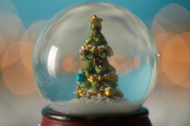 gros plan de boule de neige avec arbre de Noël debout sur le bleu dans la neige avec des branches d'épinette et des lumières bokeh
  - Photo, image