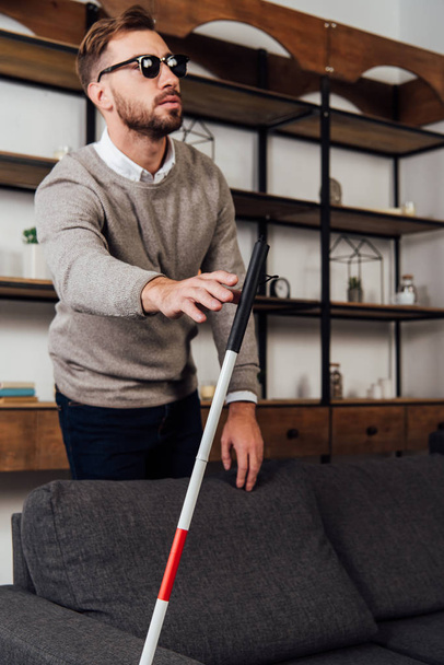 Blind man pulling hand to walking stick in living room - Foto, afbeelding