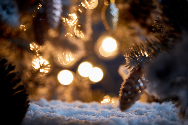 primer plano del árbol de Navidad con bolas de Navidad decorativas en la nieve con luces borrosas en la oscuridad
  - Foto, imagen