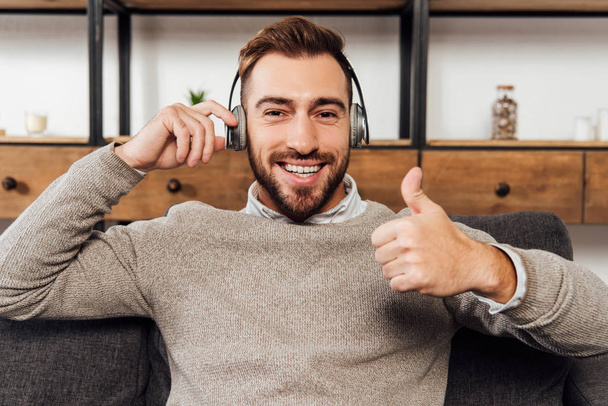 Man in headphones smiling at camera and showing thumb up gesture - Foto, Bild