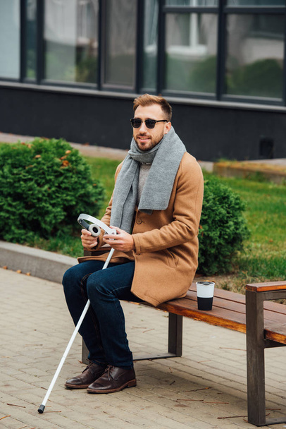 Blind man holding headphones while sitting on bench - Foto, afbeelding